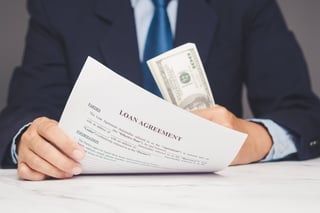 Document labeled Loan Agreement held beside hundred-dollar bills