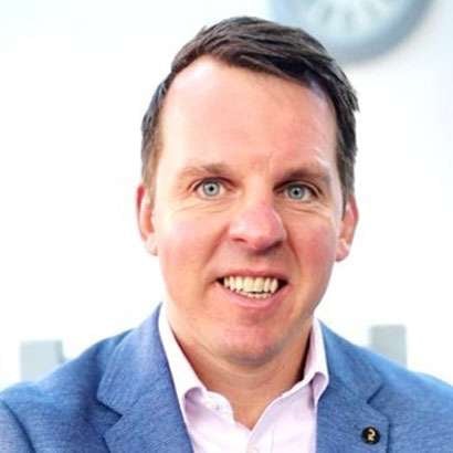 Portrait of a smiling man in a blue blazer and light pink shirt against a light background