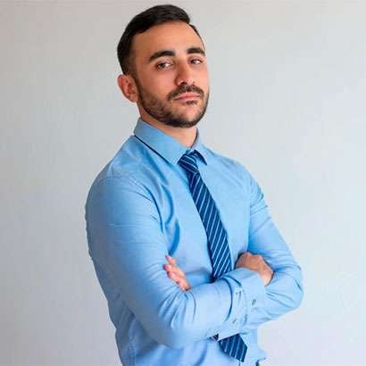 Professional man in light blue dress shirt and tie standing with arms crossed against white background