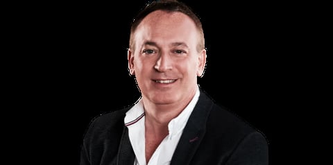Professional headshot of a man in a black blazer and white shirt, smiling at the camera against a dark background